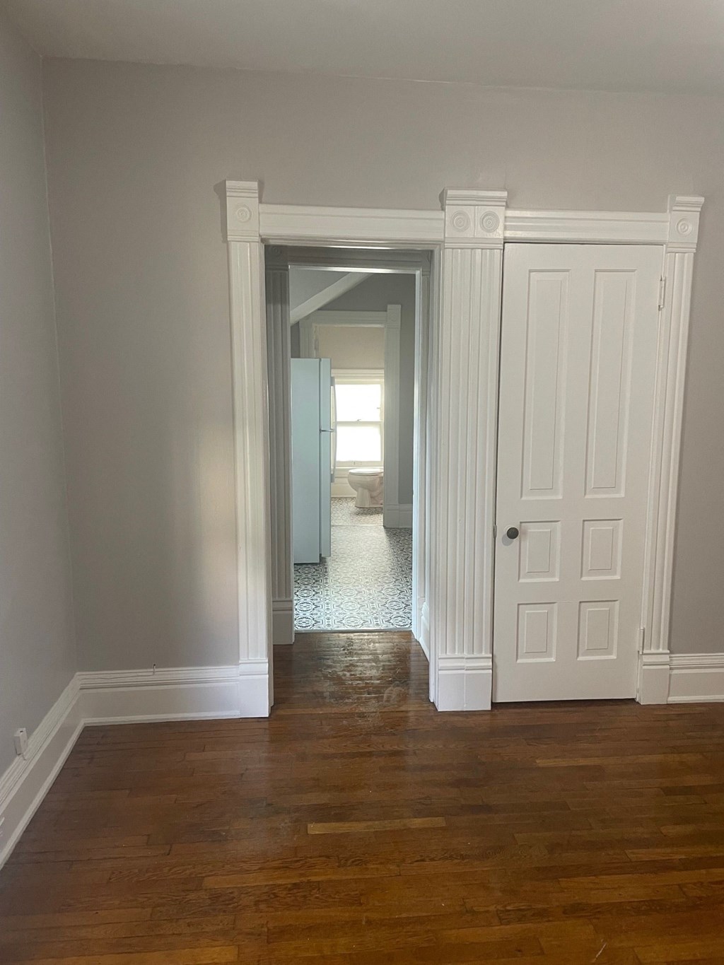 a bedroom with a door to a hallway and a closet with a refrigerator