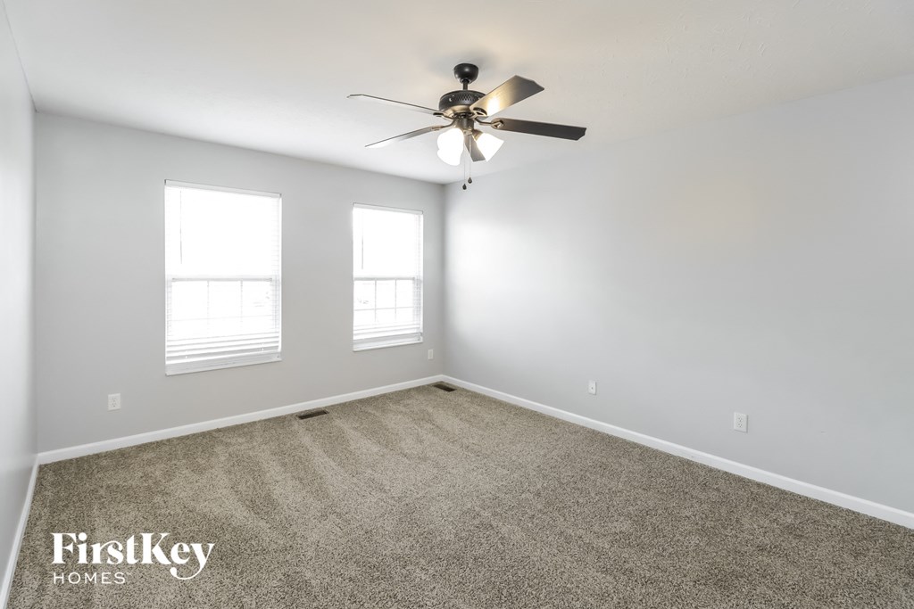 an empty room with a ceiling fan and two windows