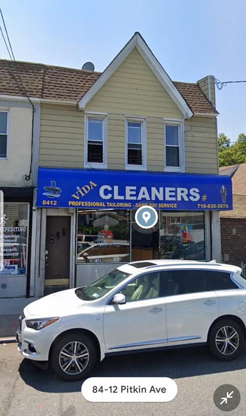 A white car is parked in front of a building that has a blue sign that says "Vida Cleaners".