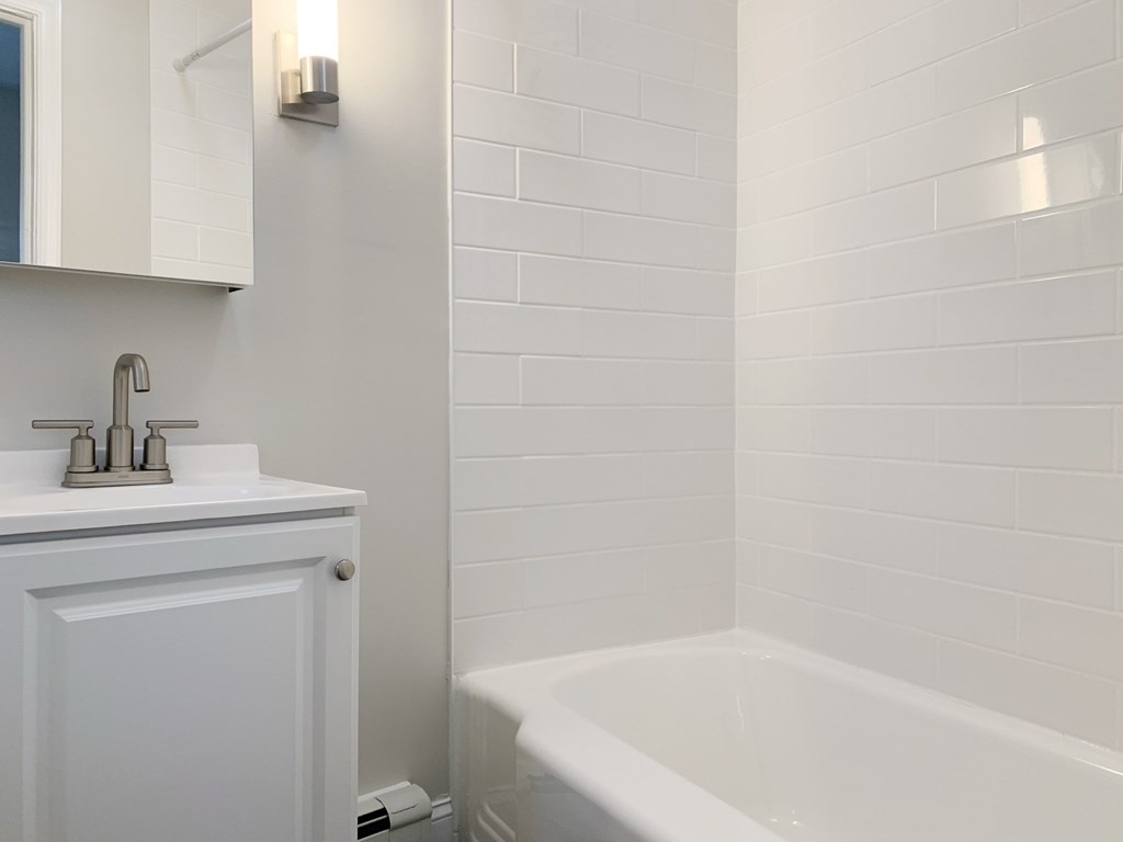 a white bathroom with a tub and a sink and a mirror
