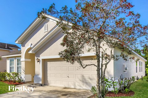 A house with a white garage door and a tree with red leaves in front of it.