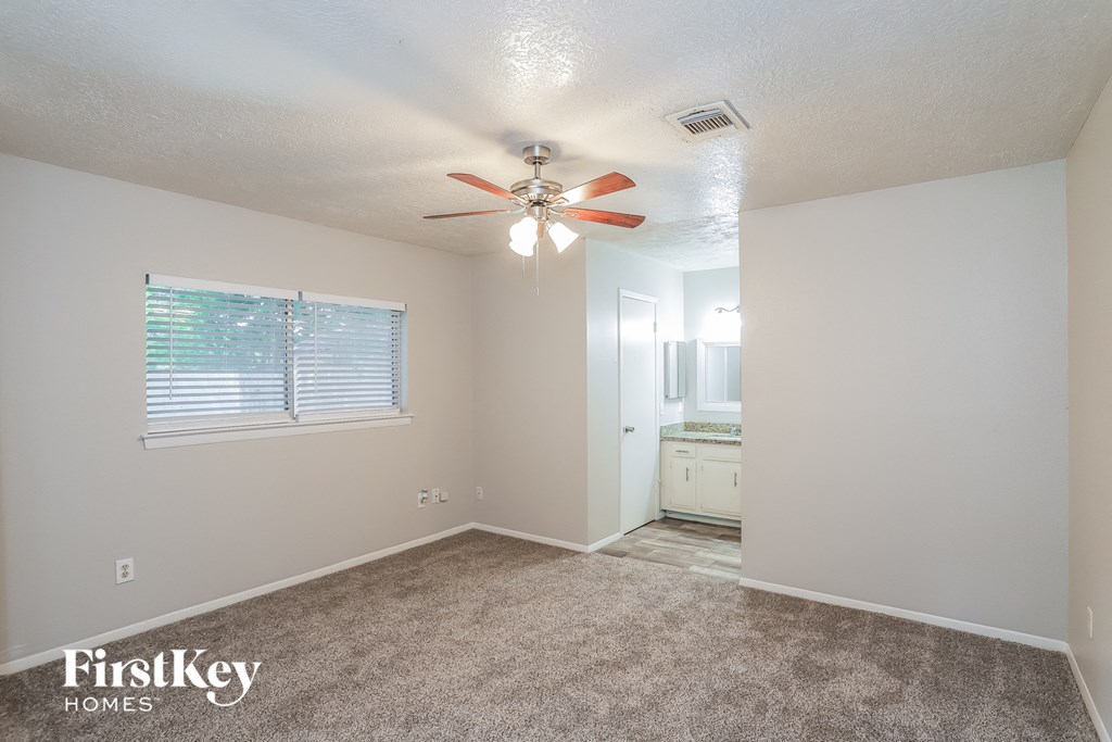 A room with a carpet floor, a ceiling fan, and a window with blinds.