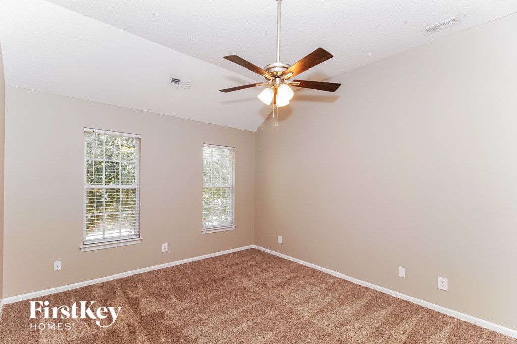 A room with a ceiling fan and two windows.