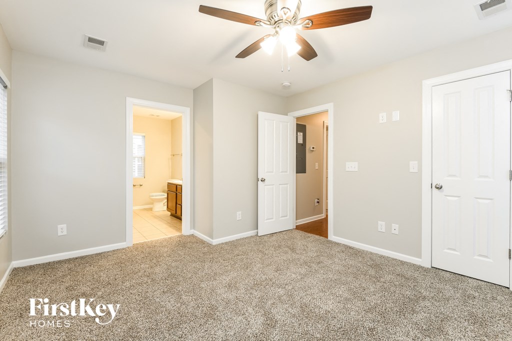 an empty living room with a ceiling fan and a door to a bathroom
