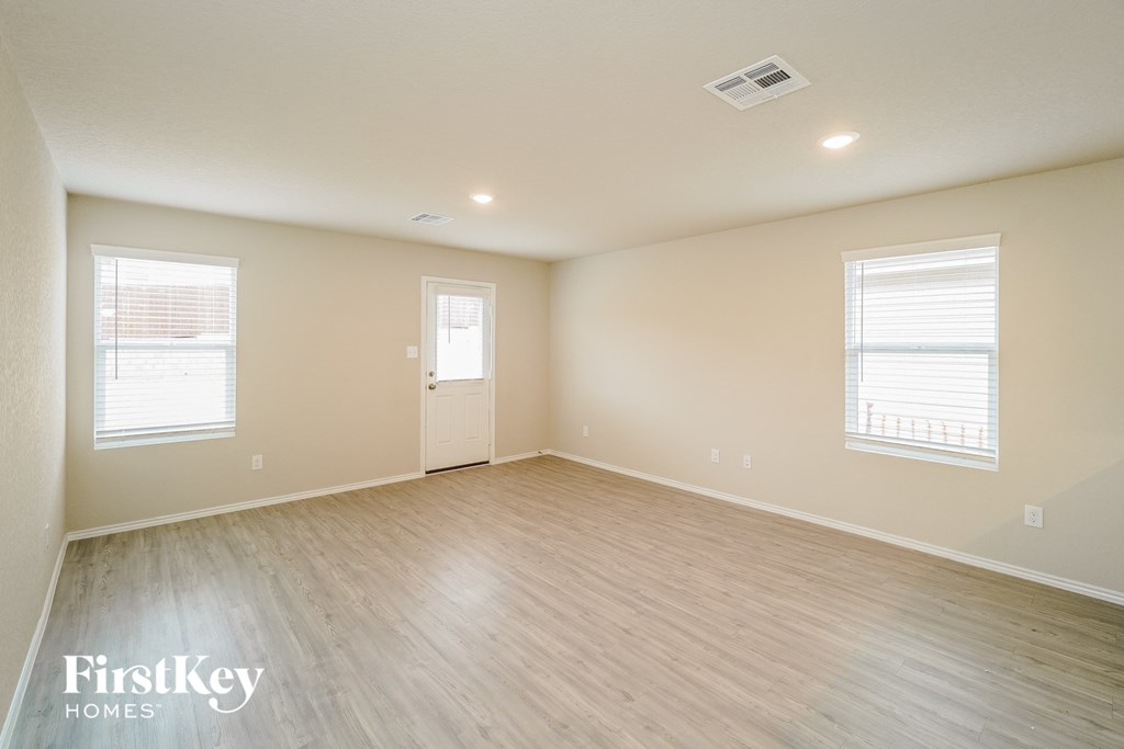 A spacious room with wooden flooring and two windows.