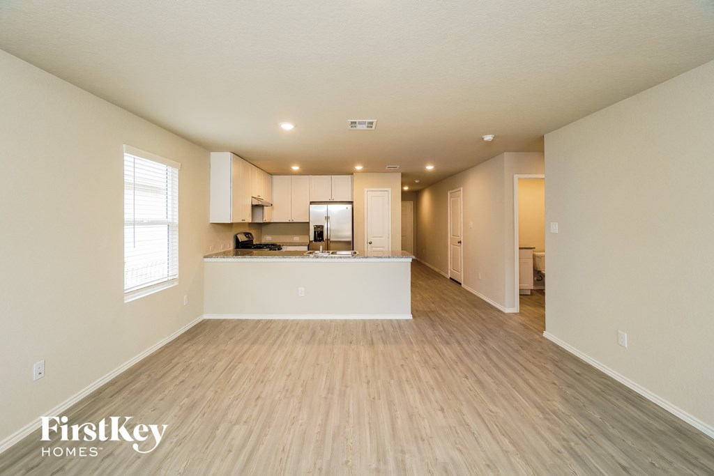 A spacious, empty room with wooden floors and a kitchen area in the background.