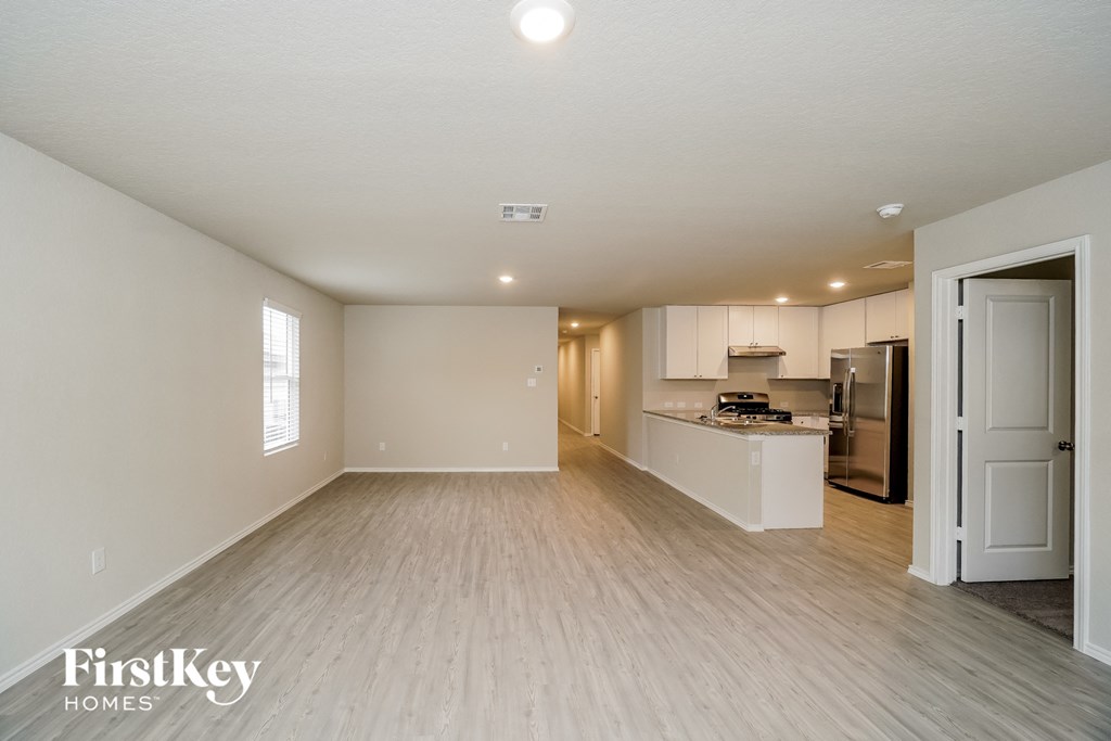 A spacious empty room with a kitchen area in the background.