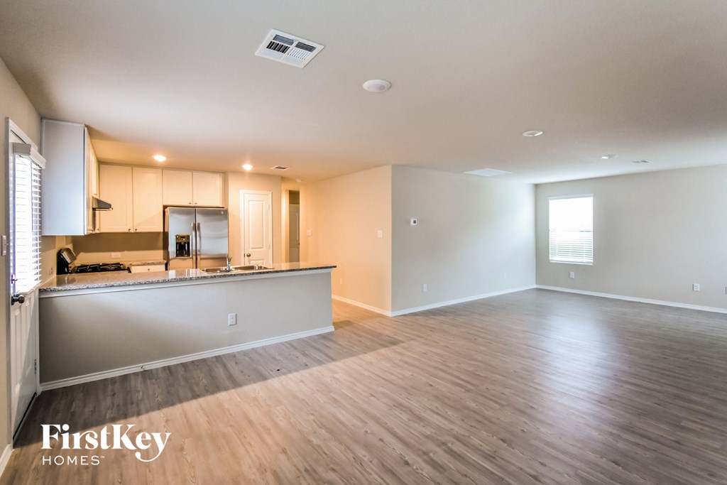 A spacious, empty room with wooden flooring and a kitchen area in the background.