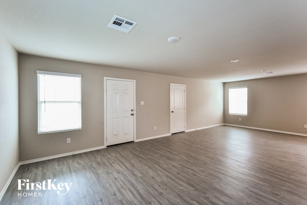 A spacious room with wooden flooring and two windows.