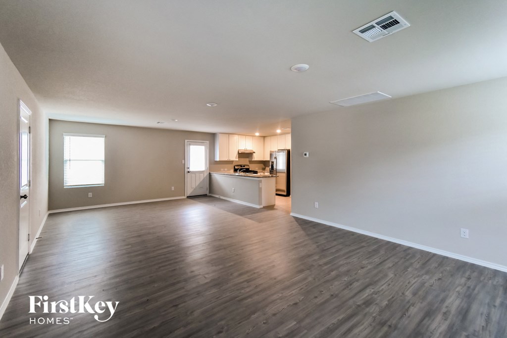 A spacious room with wooden flooring and a kitchenette in the background.