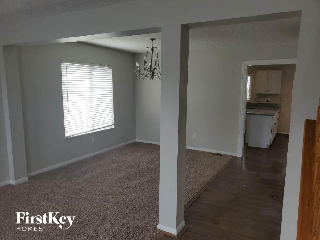 an empty living room with a kitchen in the background