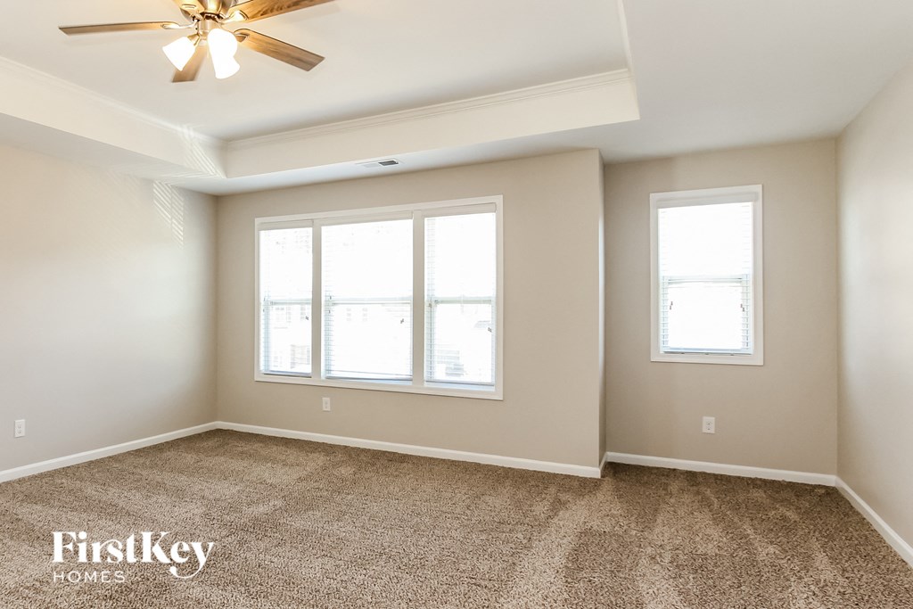 an empty living room with three windows and a ceiling fan