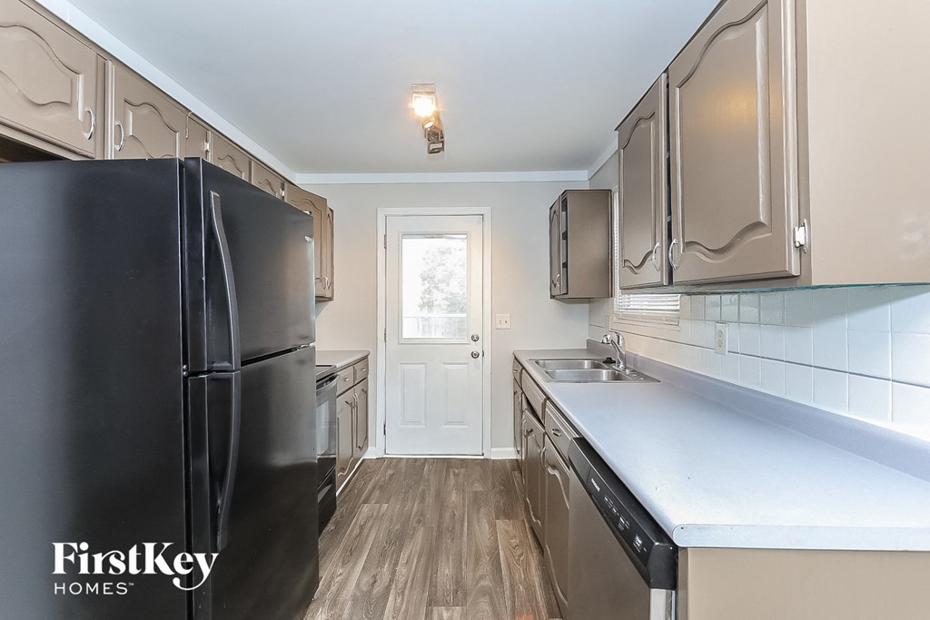 A kitchen with a black fridge and wooden floors.