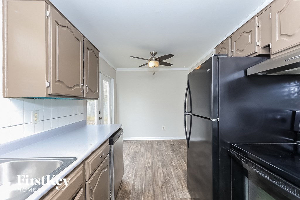 A kitchen with a black refrigerator, wooden floors, and beige cabinets.