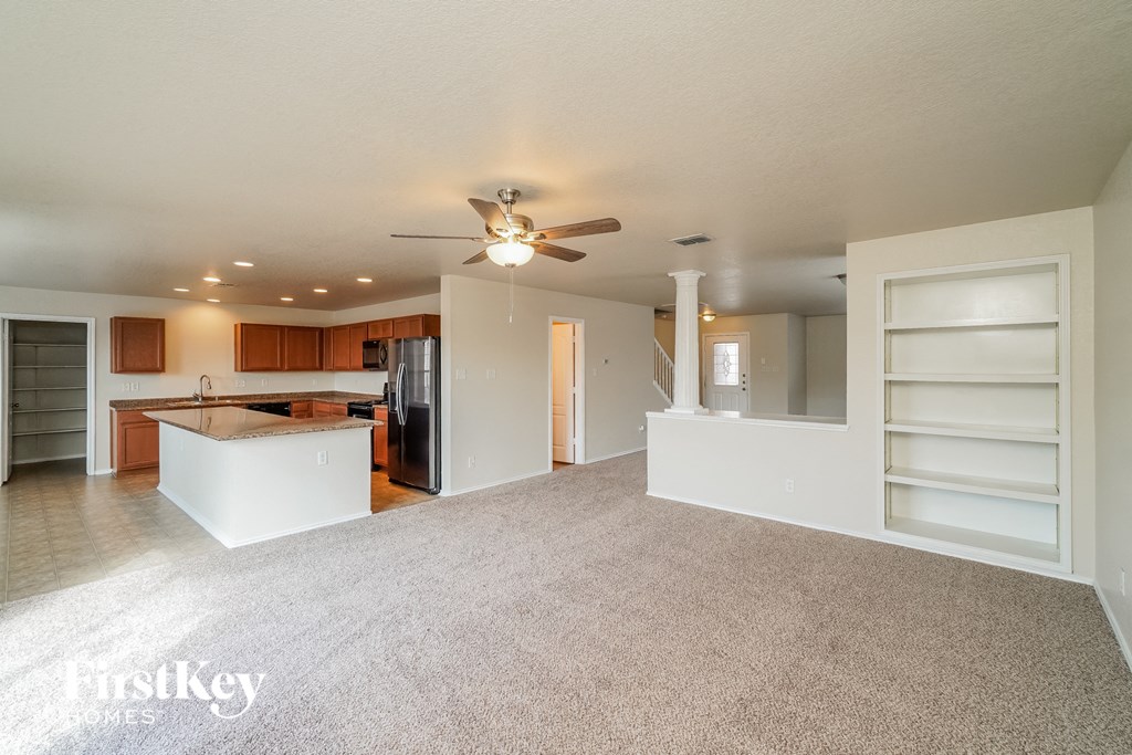 an empty living room with a kitchen and a ceiling fan