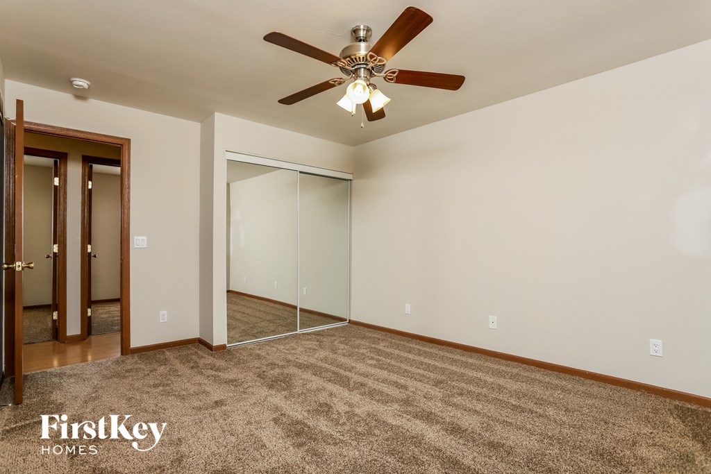 an empty living room with a ceiling fan and a mirrored closet