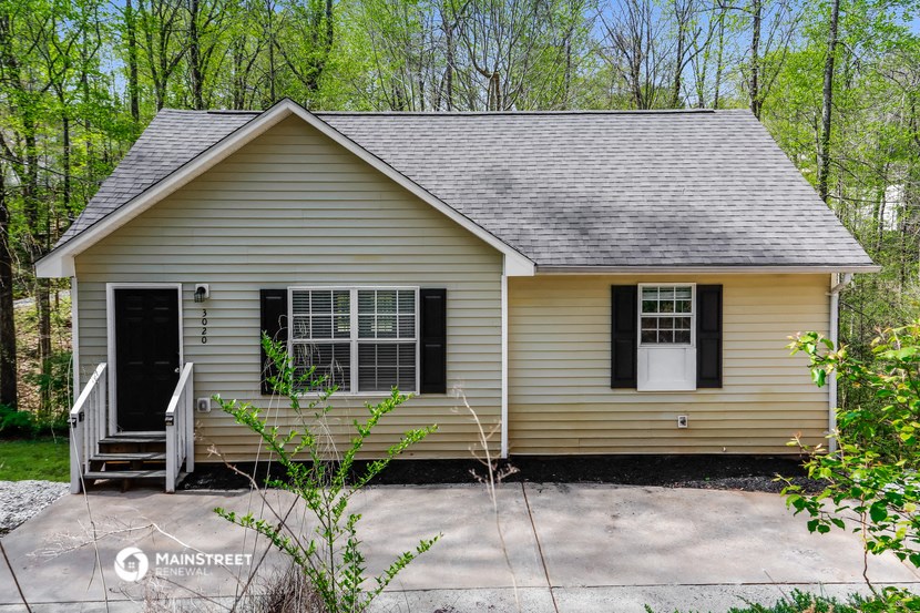 the front of a yellow house with a porch and a driveway