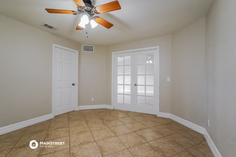 an empty living room with two doors and a ceiling fan