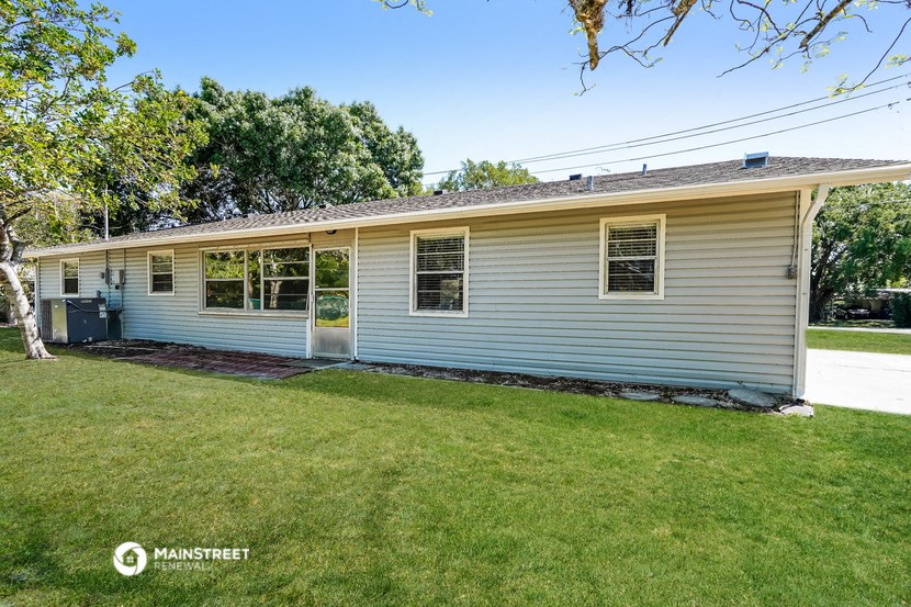 the front of a white house with a lawn and trees