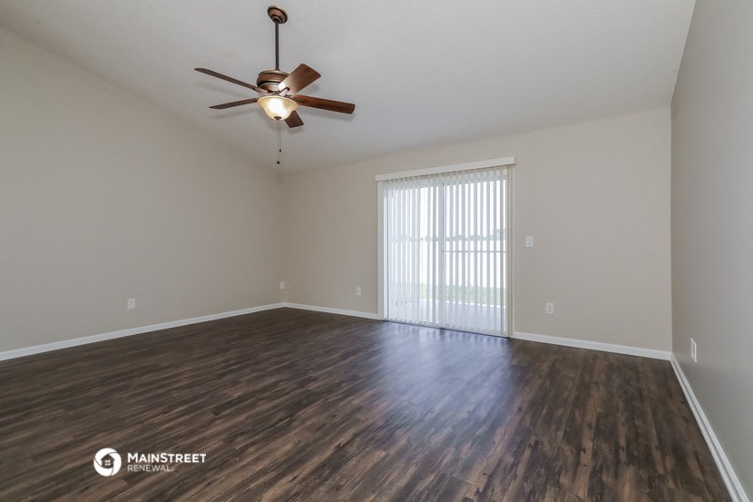the spacious living room with wood flooring and a ceiling fan