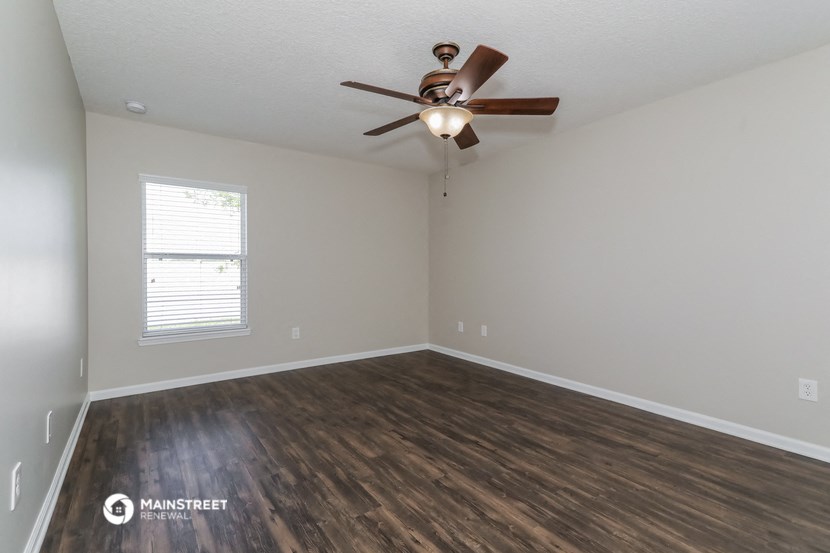 the spacious living room with hardwood flooring and a ceiling fan