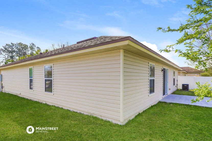 a small white house with tan siding on the side of a lawn