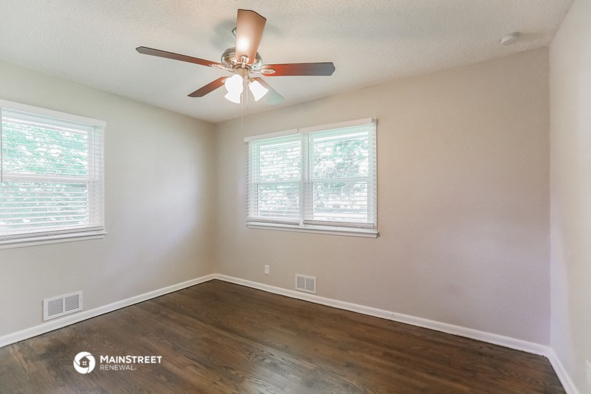 an empty room with a ceiling fan and two windows
