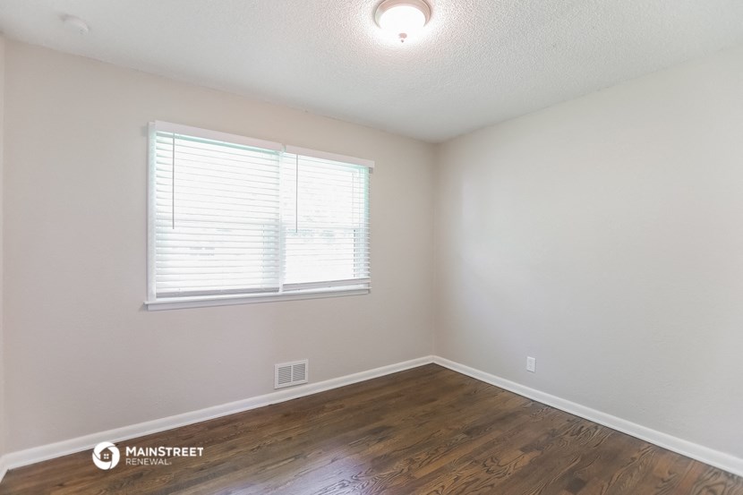 the spacious living room with wood flooring and a window