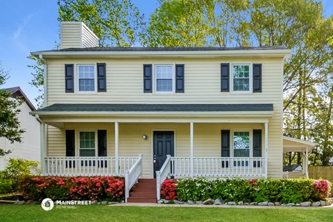 a yellow house with a white porch and a black door