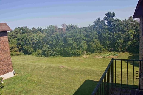 A view from a balcony overlooking a lush green lawn and trees.