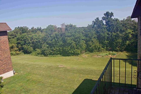 A view from a balcony overlooking a lush green lawn and trees.