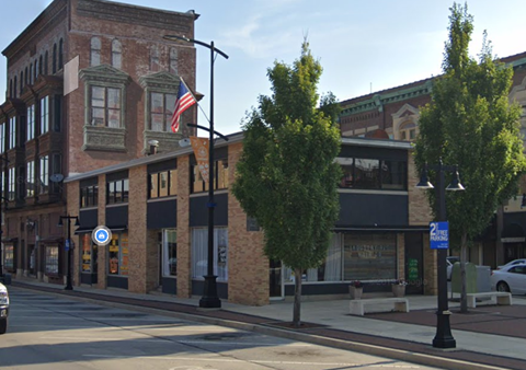 A street view of a city with a building on the left and a tree in the middle.