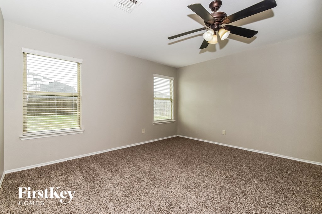 an empty bedroom with a ceiling fan and two windows