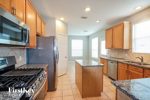 A kitchen with a black refrigerator, a black stove, wooden cabinets, and a granite countertop.