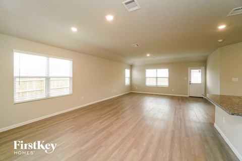 A spacious room with wooden floors and a kitchen area in the background.