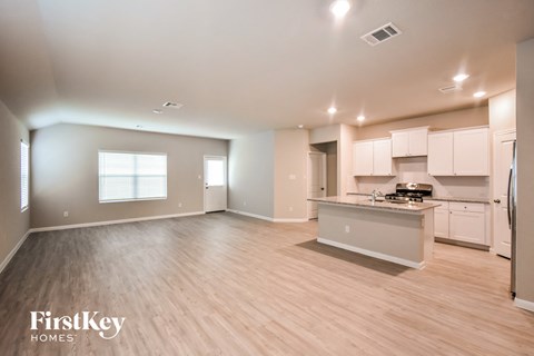 an open kitchen and living room with wood flooring and white cabinets