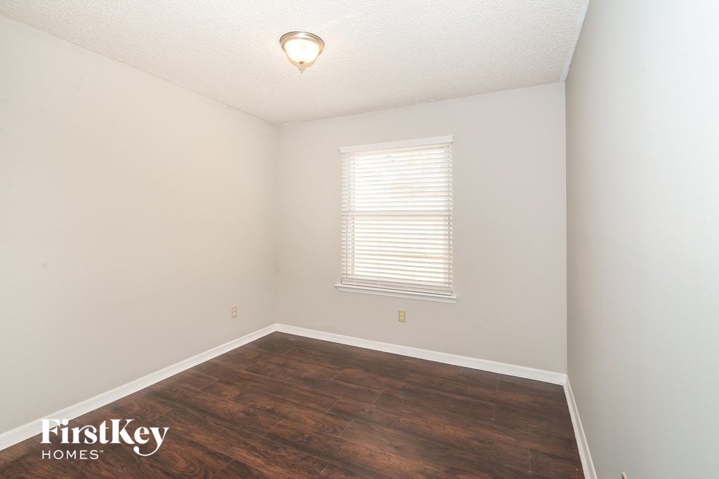 a bedroom with a wood floor and white walls and a window