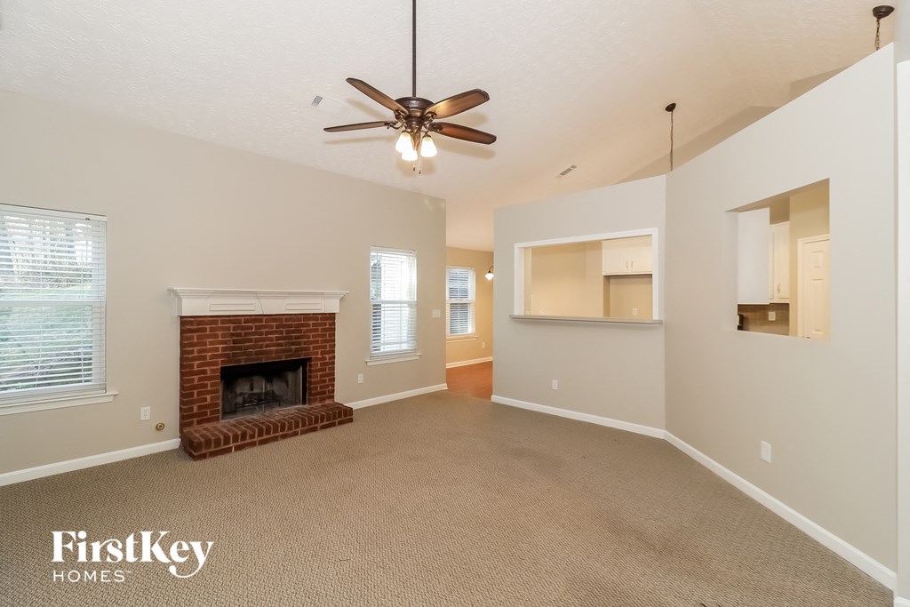 an empty living room with a brick fireplace and a ceiling fan