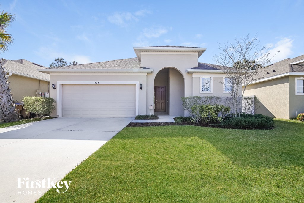 a beige house with a garage door and a lawn