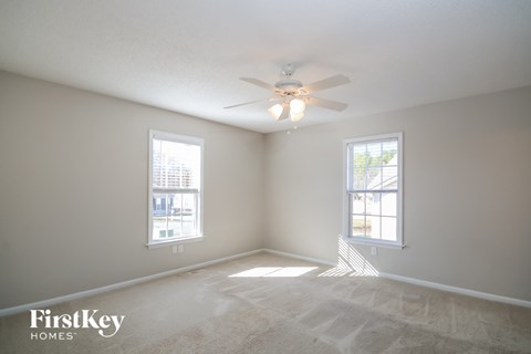 A room with a carpet floor, a ceiling fan, and two windows.