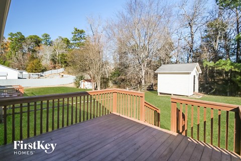 A wooden deck with a railing and a white shed in the background.