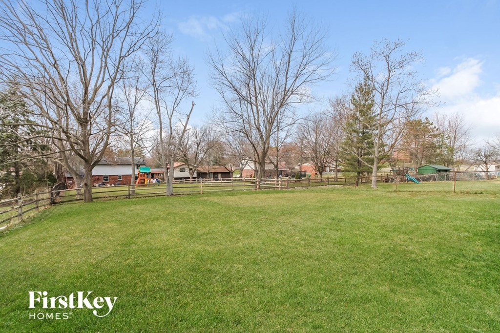 A grassy field with trees and a fence in the background.