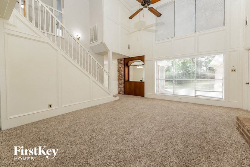 a large carpeted living room with a staircase and a ceiling fan
