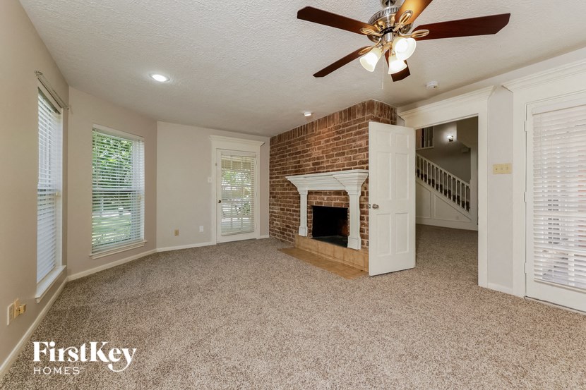 an empty living room with a brick fireplace and a ceiling fan
