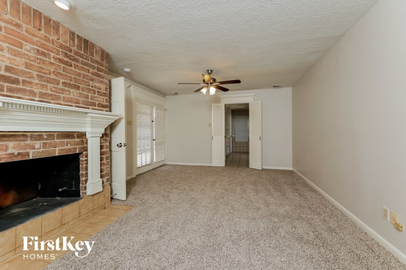 an empty living room with a brick fireplace and a ceiling fan