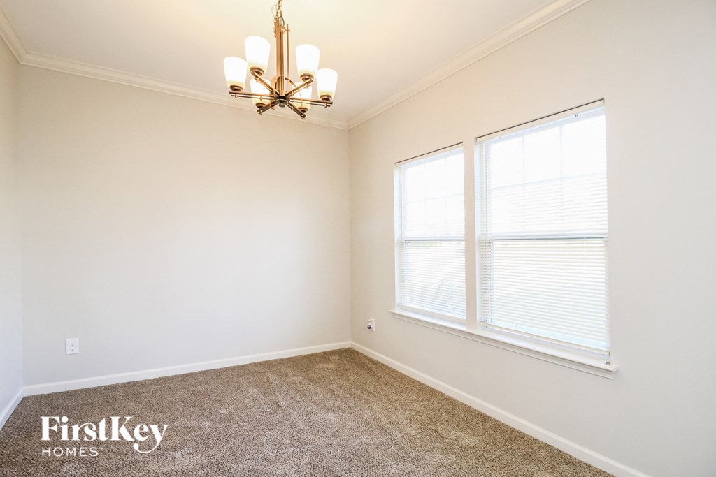 A room with a chandelier, two windows, and a carpeted floor.