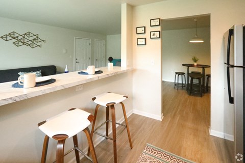 a kitchen and living room with bar stools and a refrigerator