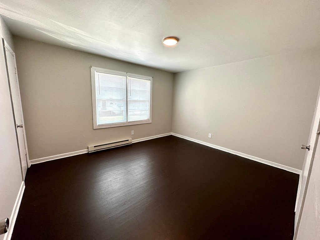 an empty room with a window and a dark wood floor