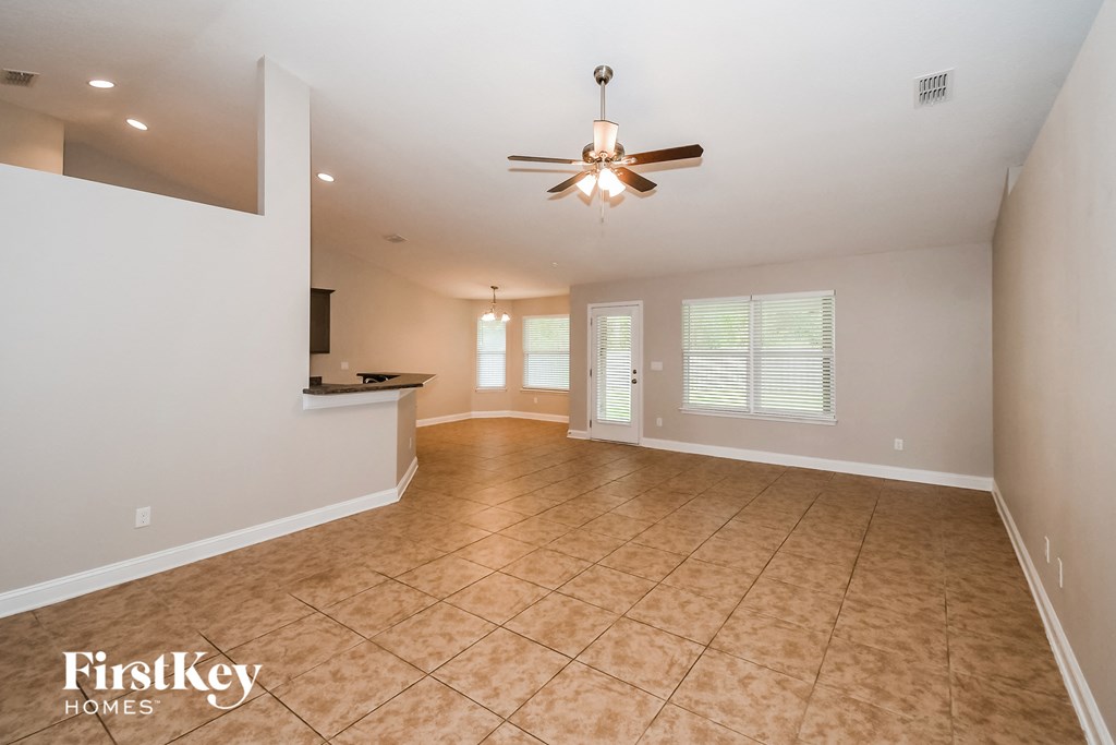 an empty living room with a ceiling fan and a kitchen