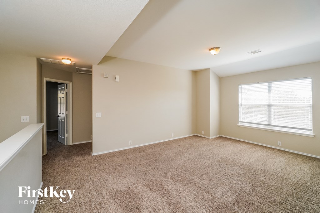A spacious room with a carpeted floor and a window with blinds.